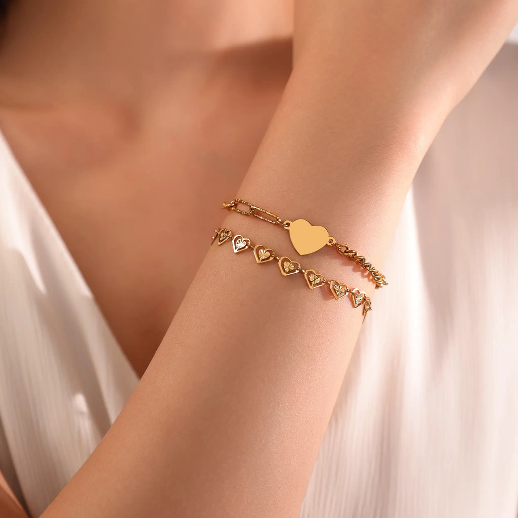 Gold bracelet stacking style featuring Vilrian asymmetric heart chain bracelet and hollow heart chain